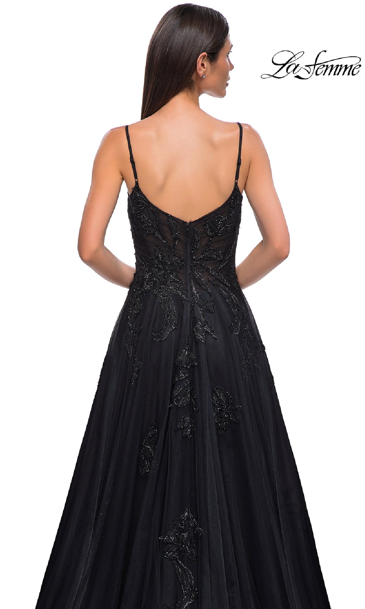 A woman with long dark hair models the La Femme 32781, a long black glitter prom dress with strappy back detail, shown from behind against a white background.